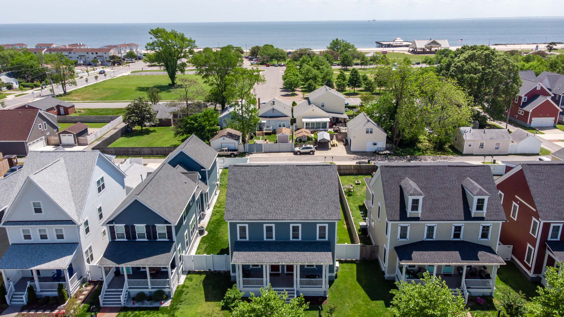 Aerial view of a blue beach home with a spacious front porch, located near the coastline.