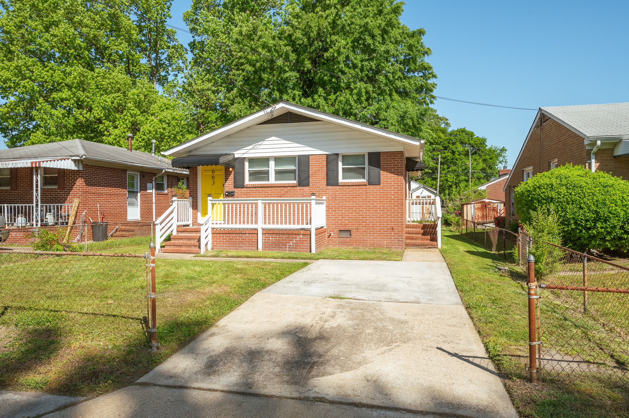 Front exterior of a red brick house with a yellow door, white railing, and a driveway.