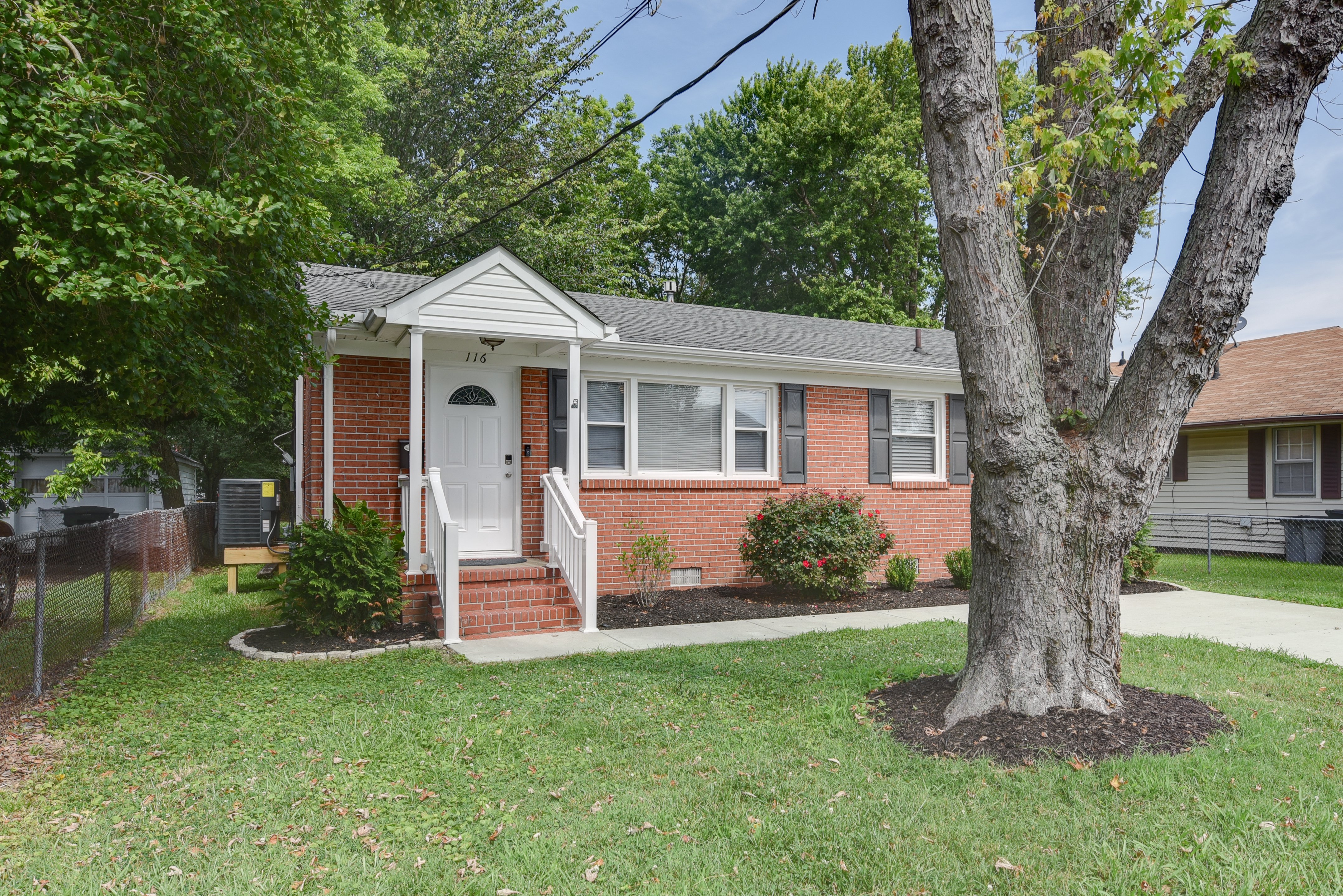 Front view of a charming brick home with a large tree in the yard